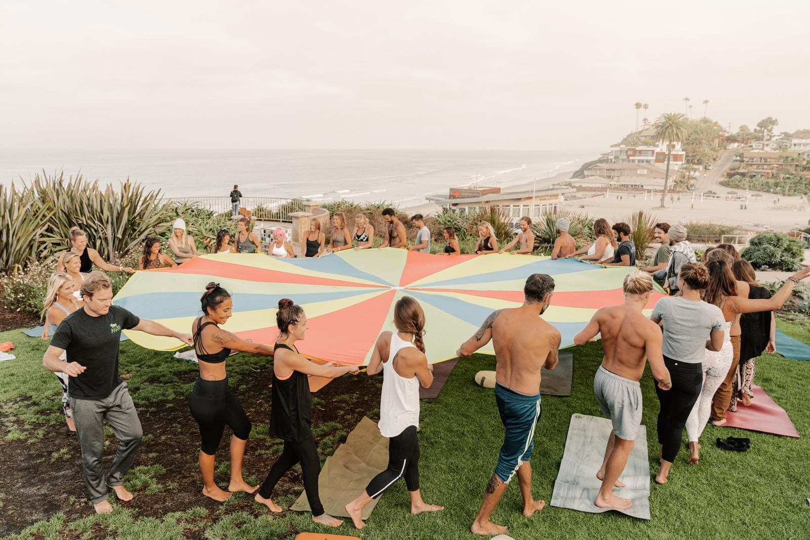 Adults holding the edges of a parachute together on a sunny lawn