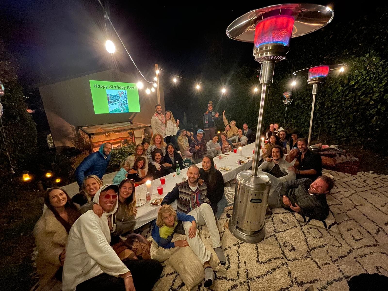 Friends gathered around a long table at night under string lights